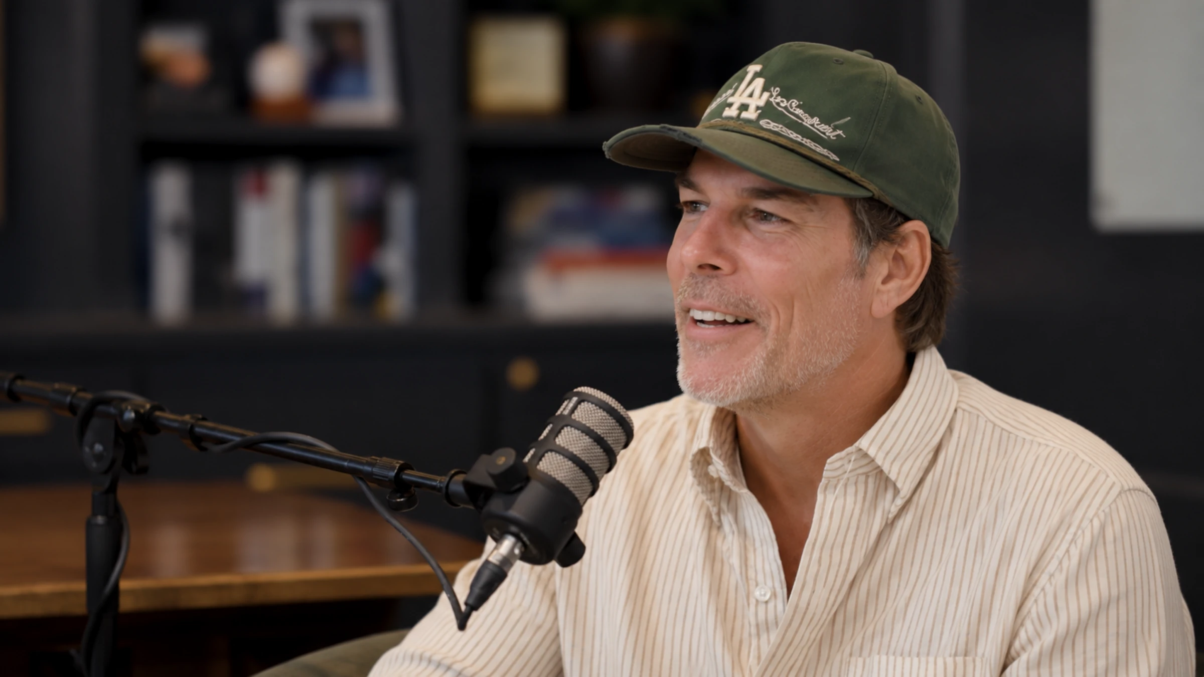 Jason Wenk wearing a green Los Angeles Dodgers cap, angled toward a podcast microphone.